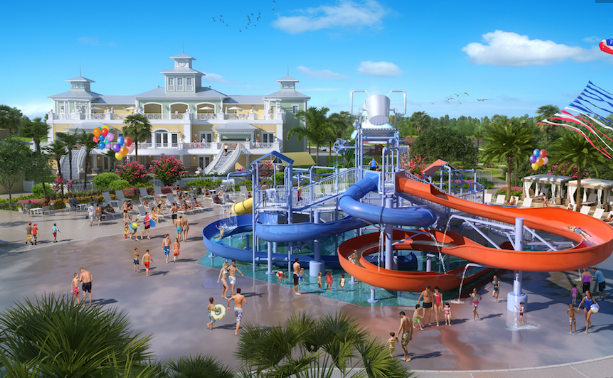 Waterpark with lots of people and a blue slide and orange slide and large bucket above. Large yellow building in the background.