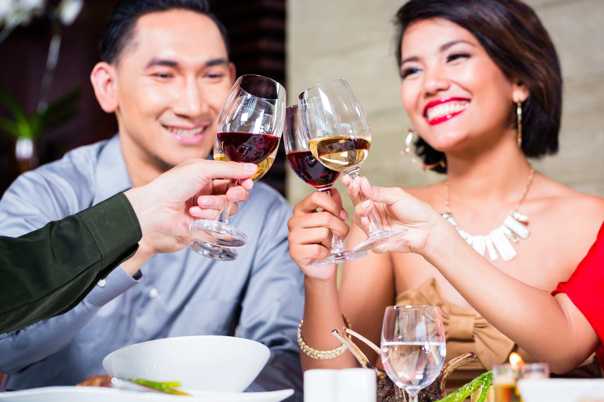 A man and woman are smiling and clinking wine glasses with another couple