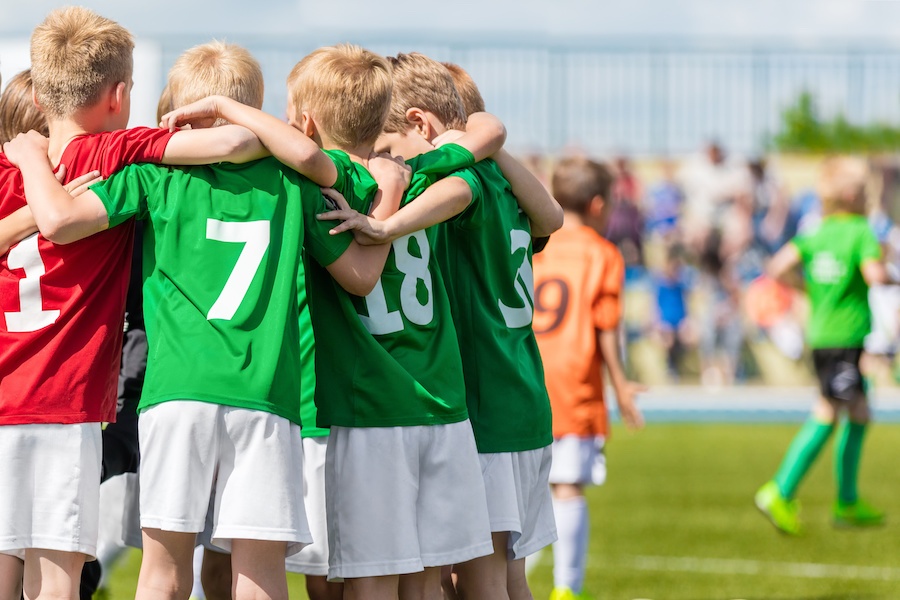 Boys in green jerseys are huddling on a soccer field with a crowd in the background.