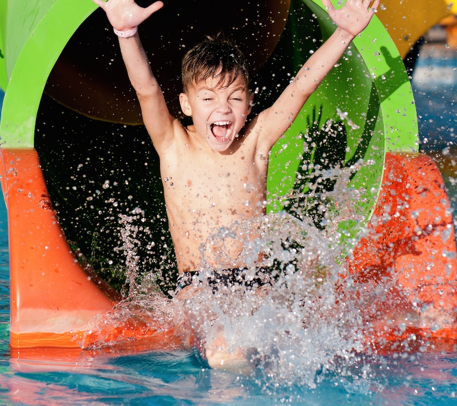 A boy throwing his hands up at the bottom of a waterslide