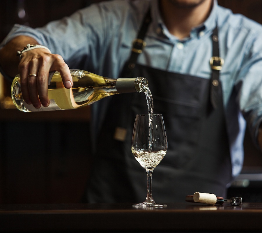 A close up of a bartender pouring a glass of white wine