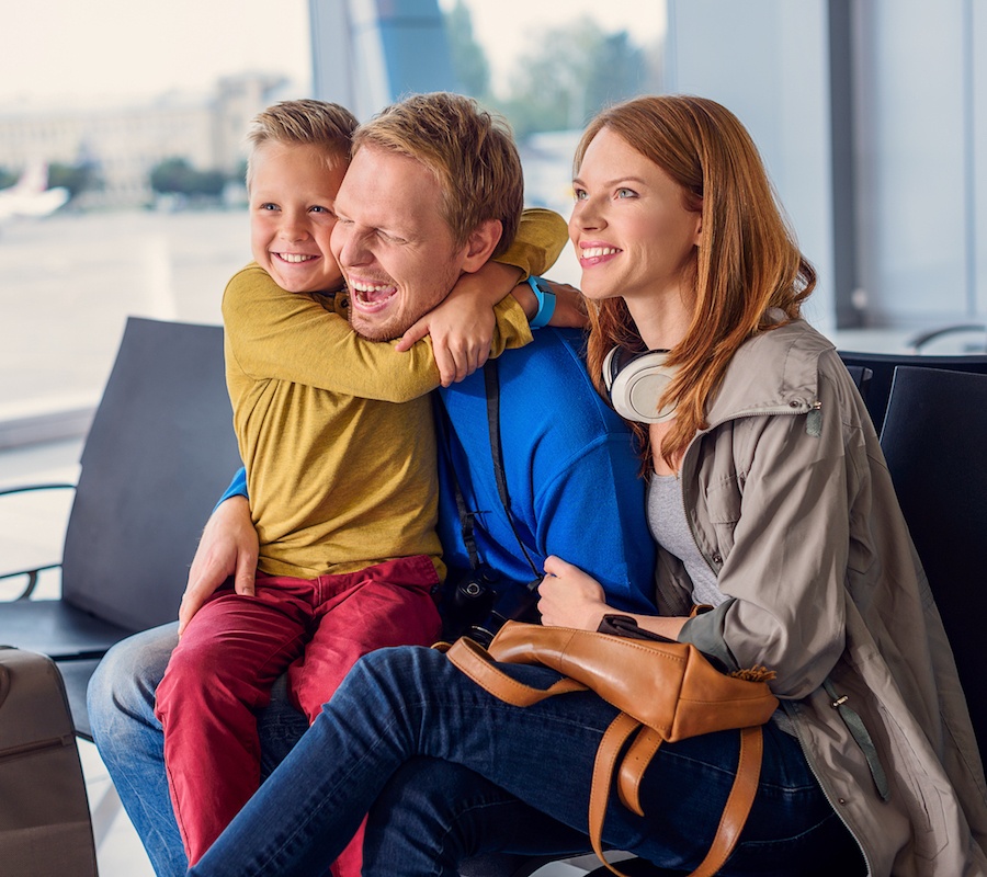 A family of three sitting at the airport, the son is sitting on his father's lap and hugging his neck