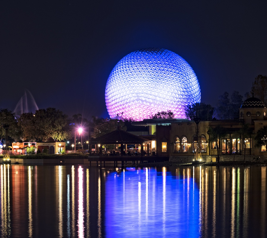 A picture at night from across the water of the light up Epcot ball. It is blue on top and pink on the bottom