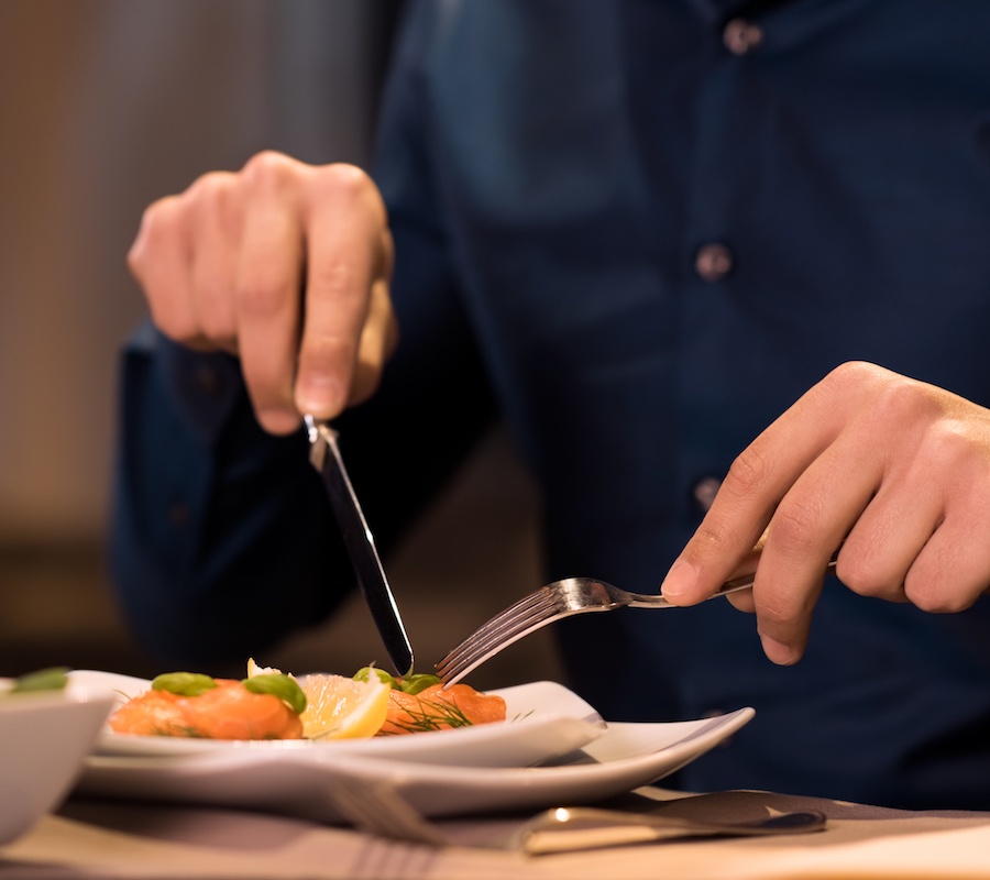A close up image of someone cutting their food on a white plate with a fork and knife