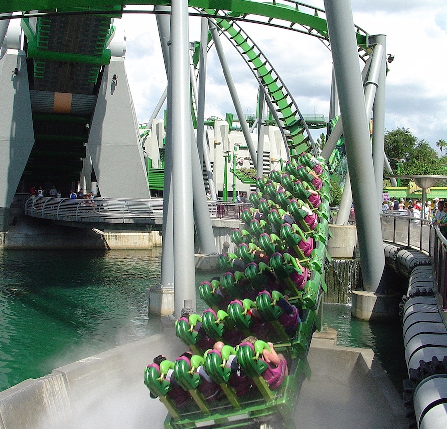 An up close picture of a green roller coaster going over water