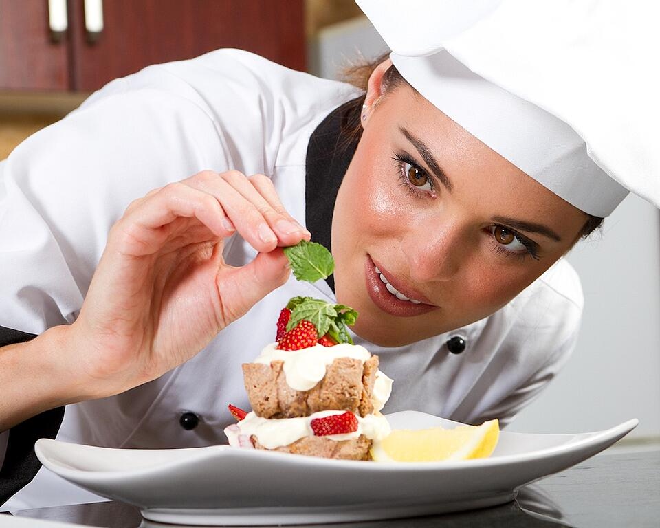 A chef is carefully putting mint on top of a strawberry short cake with a lemon on the side