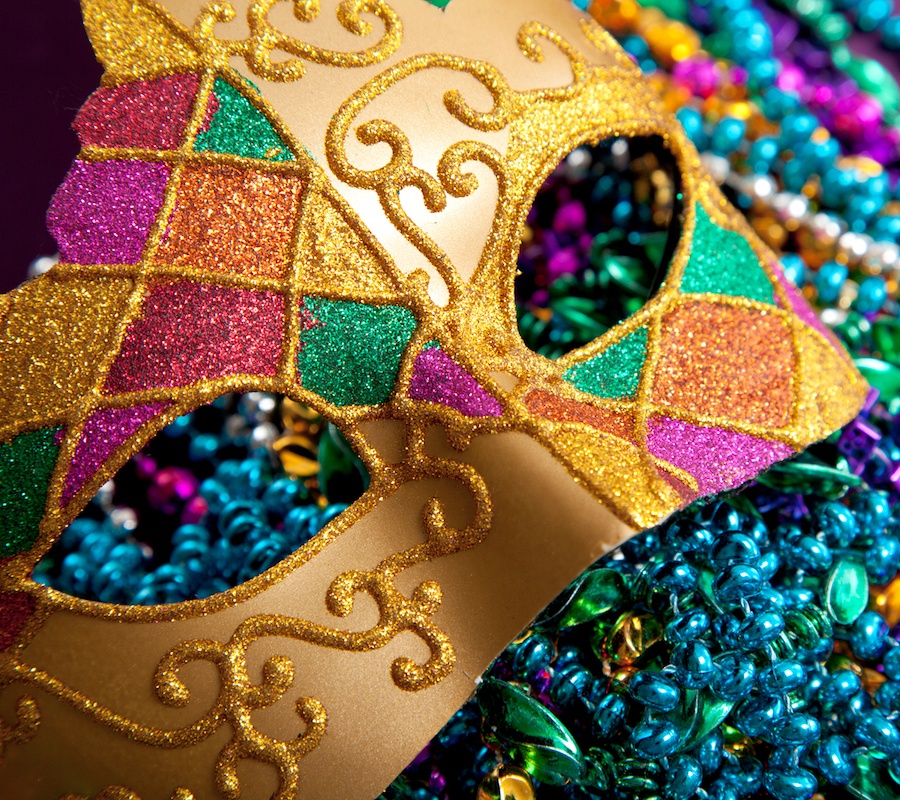 A close up image of a gold Mardi Gras mask with red, orange, pink, yellow and green on top of different colored Mardi Gras beads