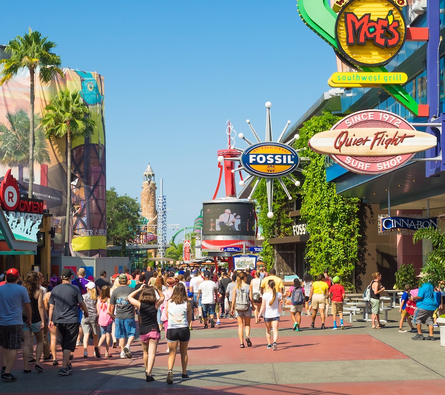 A picture of a lot of people walking around the food area, where you can see "Moe's Southwest Grill", "Fossil", "Quiet Flight Surf Shop" "Cinnabon" and more