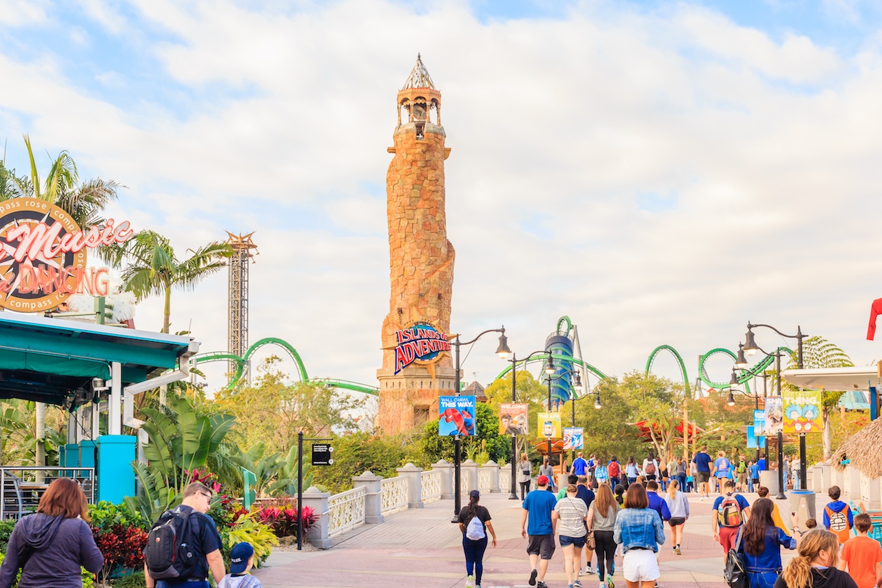 A picture of the park in front of the ride "Islands of Adventure" which is a tall brick tower. The park is filled with people.