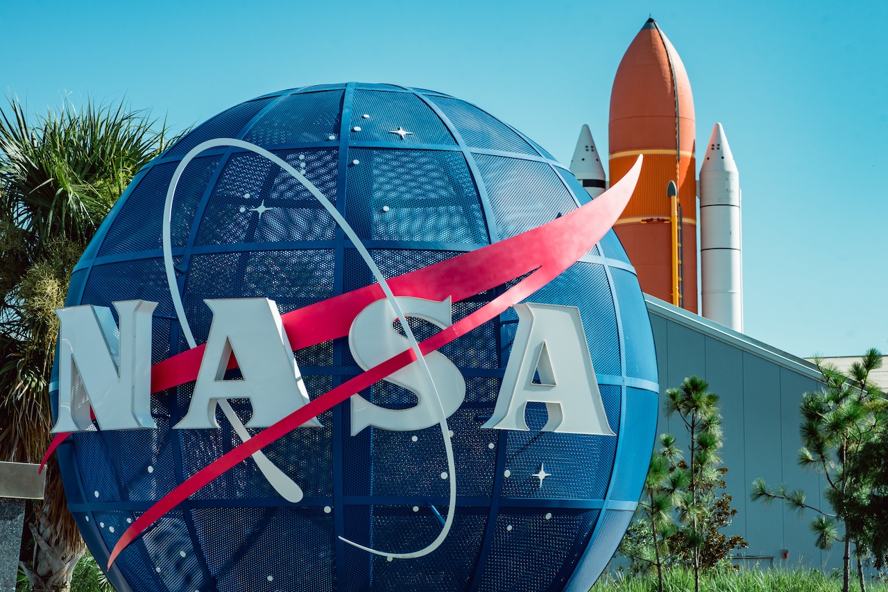 A close up of the NASA logo on a big blue ball with a rocket in the background.