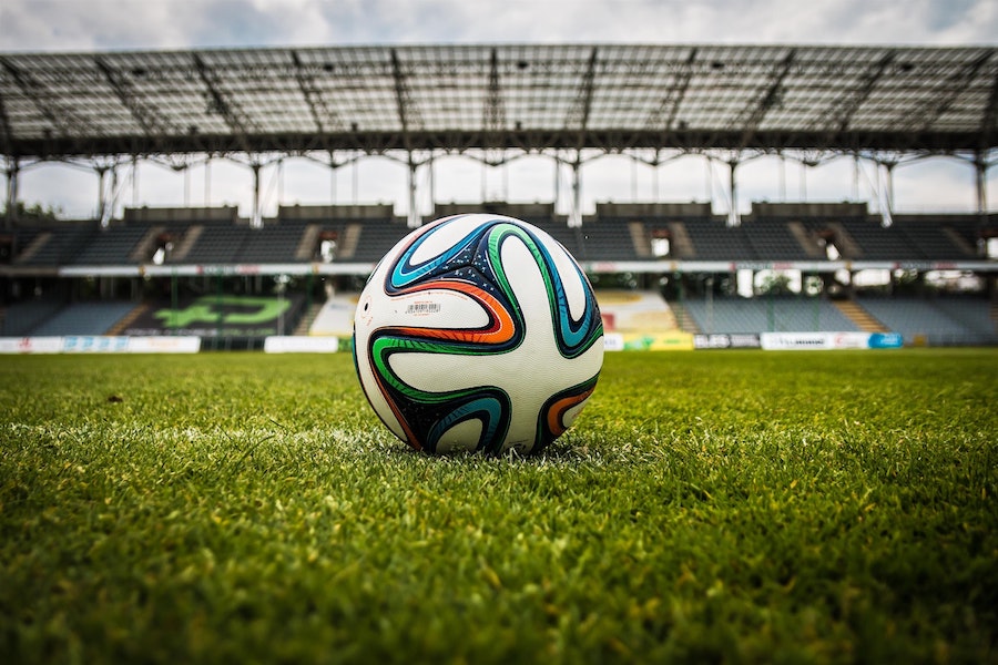 one soccer ball on turf in an empty stadium. Ball is white with black, orange, green and blue swirled designs