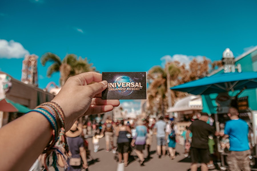 An arm outstretched holding the Universal Orlando Resort ticket in front of the resort where many people are walking around