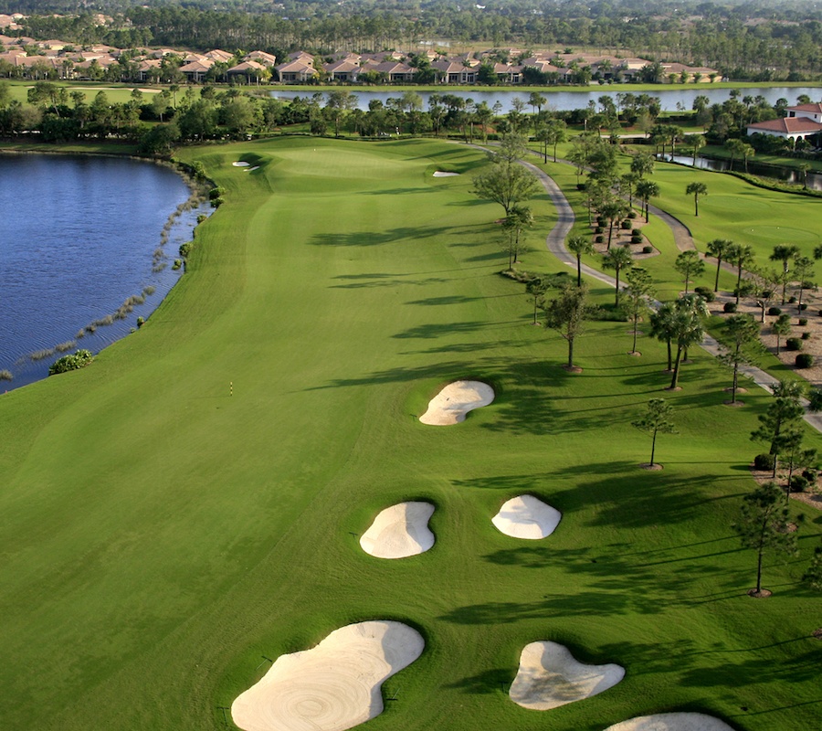 Birdseye view of the golf course with sand pits and water to the left, palm trees to the right, and houses in the background